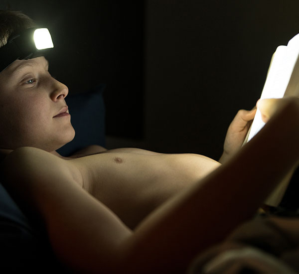 Poika lukee kirjaa otsalampun valossa