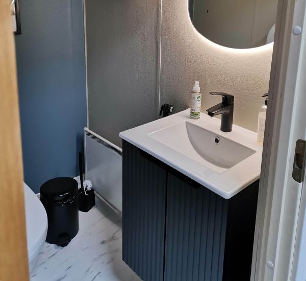 Tumma allaskaappi ja valkoinen pesuallas toimiston WC:ssä